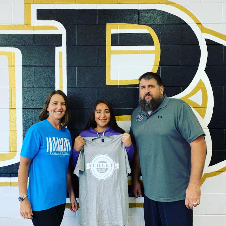 Athlete of the Week winner, Kaci Phelps, holding up her shirt. Also pictured are Kris Siegenthaler with Impact and Chad Stanton, Athletic Director at Beggs.
