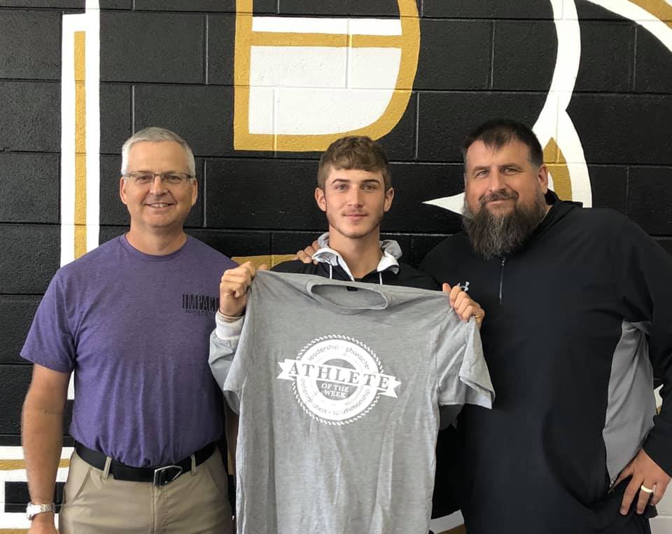 Athlete of the Week winner, Easton Davis pictured holding up his shirt with coach Chad Stanton and Michael Siegenthaler.